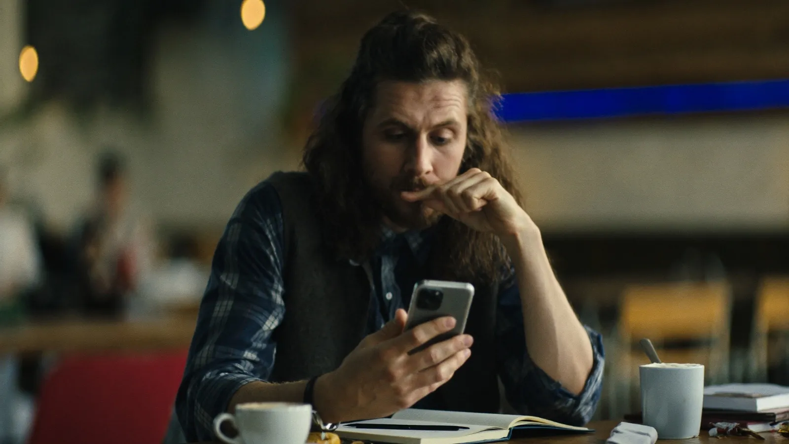 Smulkaus verslo savininkas telefone peržiūri Facebook reklamos rezultatus prie kavinės staliuko