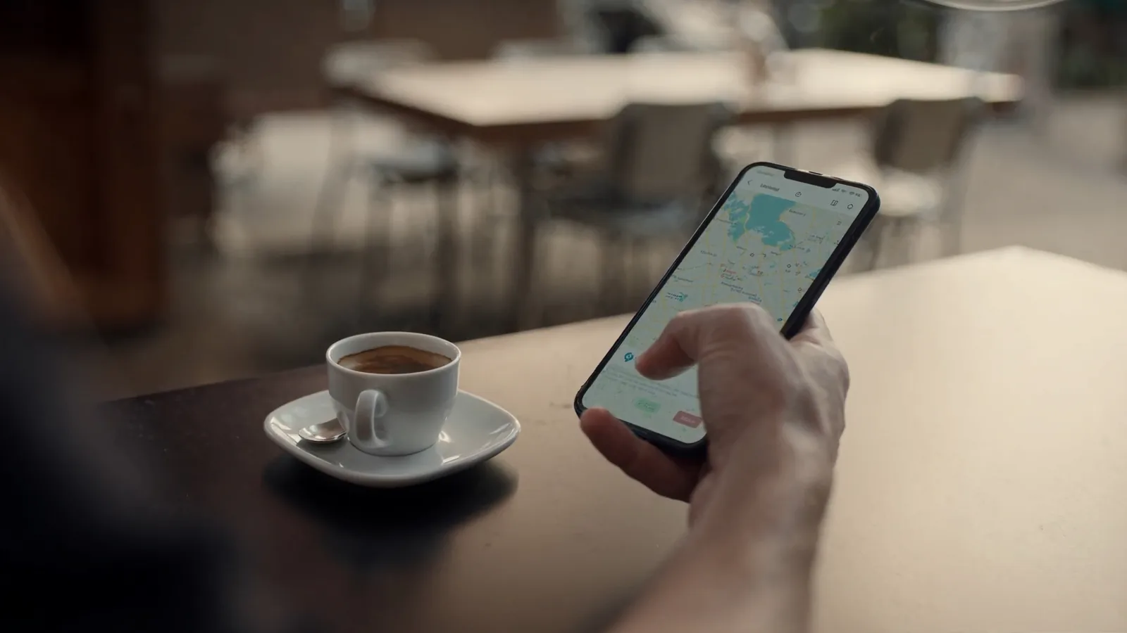 Išmanusis telefonas su atidarytu žemėlapiu ir verslo vietos žymekliu ant kavinės staliuko