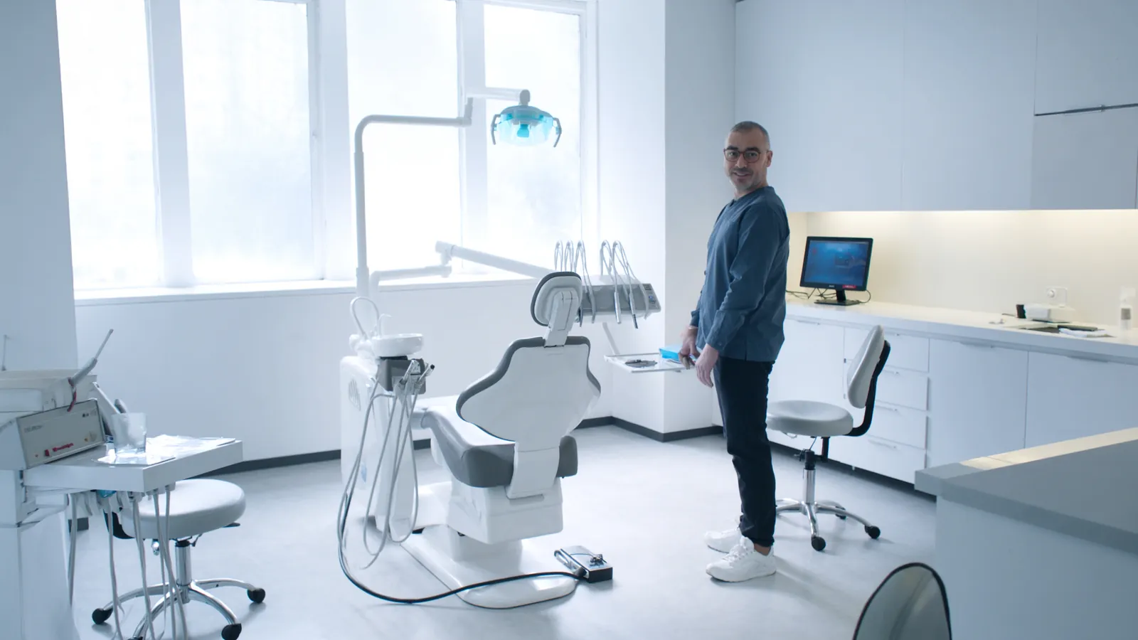 Šviesus modernus odontologijos kabinetas su odontologine kėde, moderni įranga ir gydytojas balta apranga