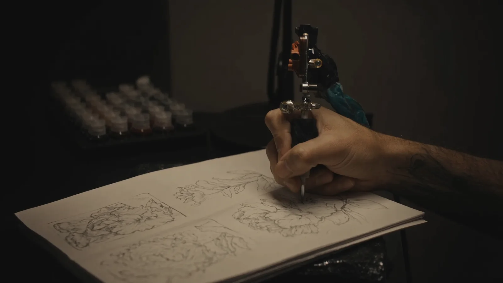Tatuiruočių studijos darbo vieta su tatuiravimo mašinėle, pigmentų buteliukais ir eskizų sąsiuviniu