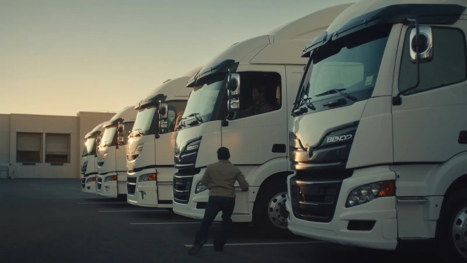 Balti vilkikai su puspriekabėmis transporto įmonės aikštelėje ankstų rytą, vairuotojas eina link kabinos