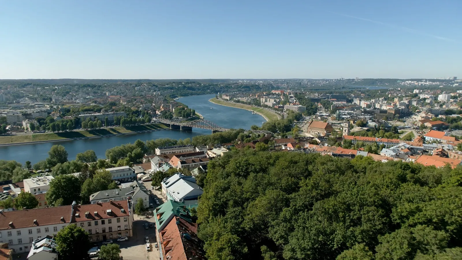Šviesus Kauno miesto vaizdas iš viršaus su senamiesčio stogais, upėmis ir moderniais pastatais saulėtą dieną